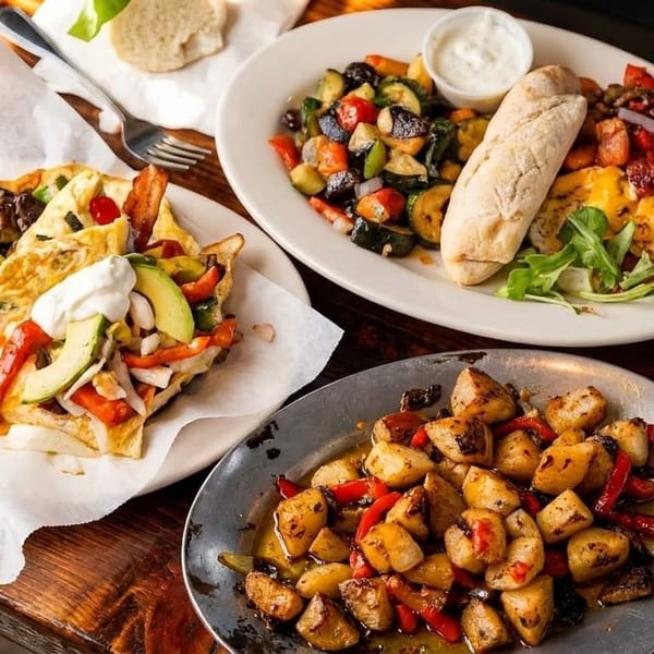 Three plates of breakfast food, including omelets, roasted vegetables, and potatoes, on a wooden table.