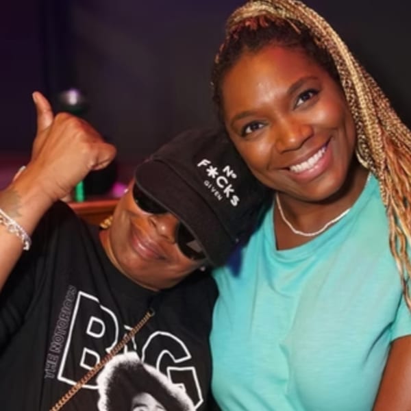 Two women smiling, one in a black cap and t-shirt, the other in a teal shirt.
