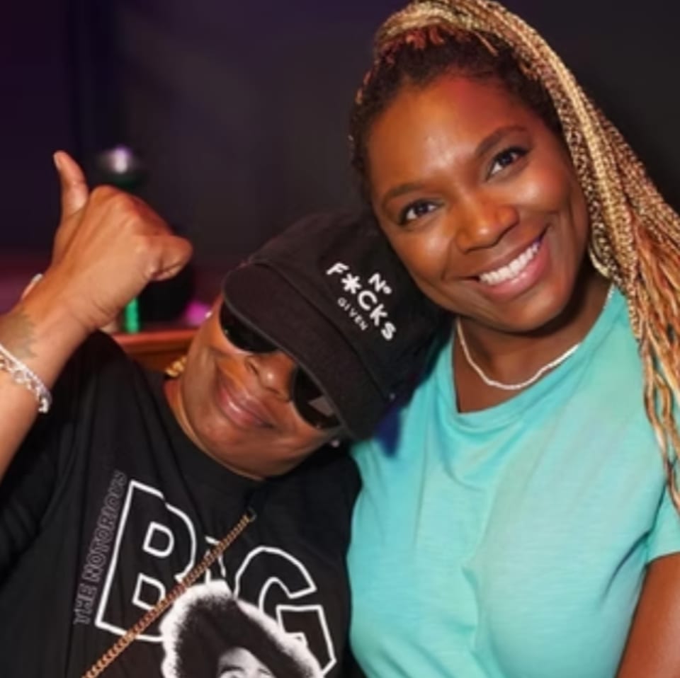 Two women smiling, one in a black cap and t-shirt, the other in a teal shirt.