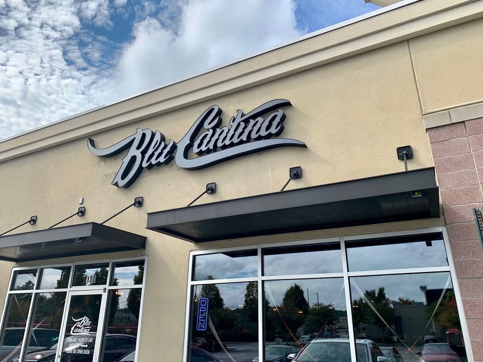 Exterior view of Blu Cantina restaurant with its sign, windows, and awnings under a cloudy sky.