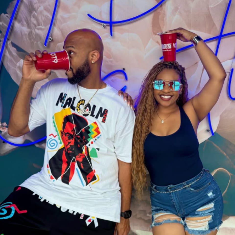 A man and woman posing with red cups, the woman balancing one on her head.