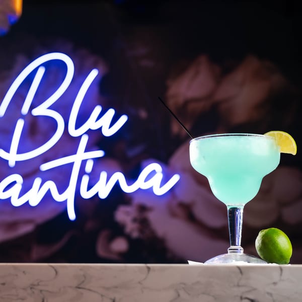 Blue margarita with lime on a marble bar, with a "Blu Cantina" neon sign in the background.