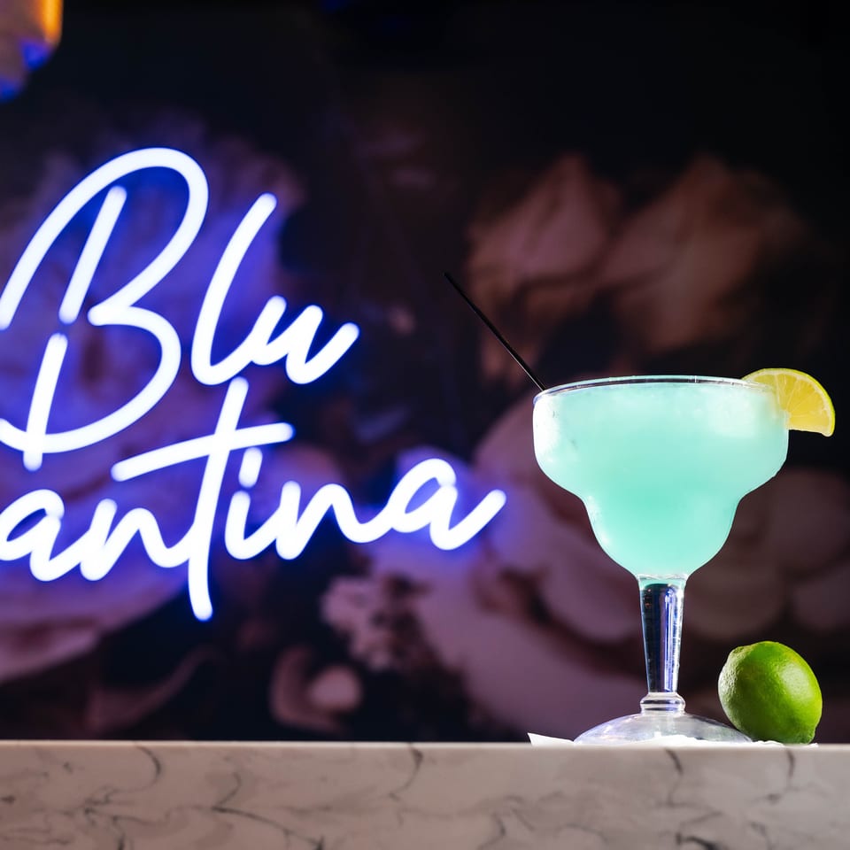 Blue margarita with lime on a marble bar, with a "Blu Cantina" neon sign in the background.