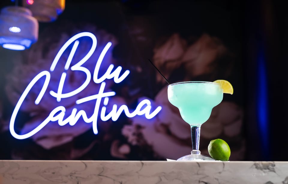 Blue margarita with lime on a marble bar, with a "Blu Cantina" neon sign in the background.